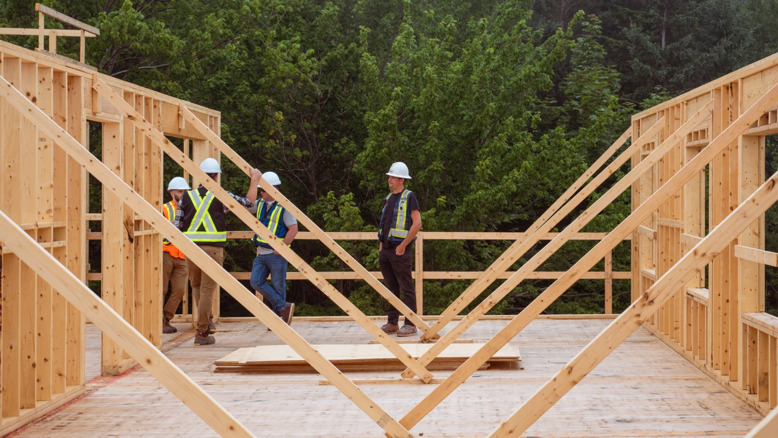 Group of construction workers and engineers wearing hard hats and high-visibility vests standing in a building under construction, engaged in a discussion.